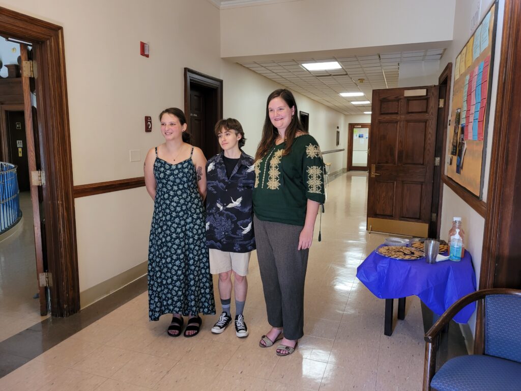 Three students standing in a hallway next to a table with snacks.
