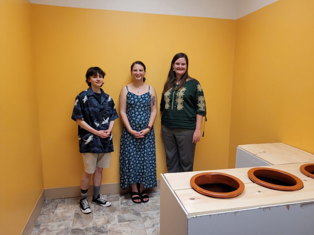 Three students stand in front of a yellow wall smiling.